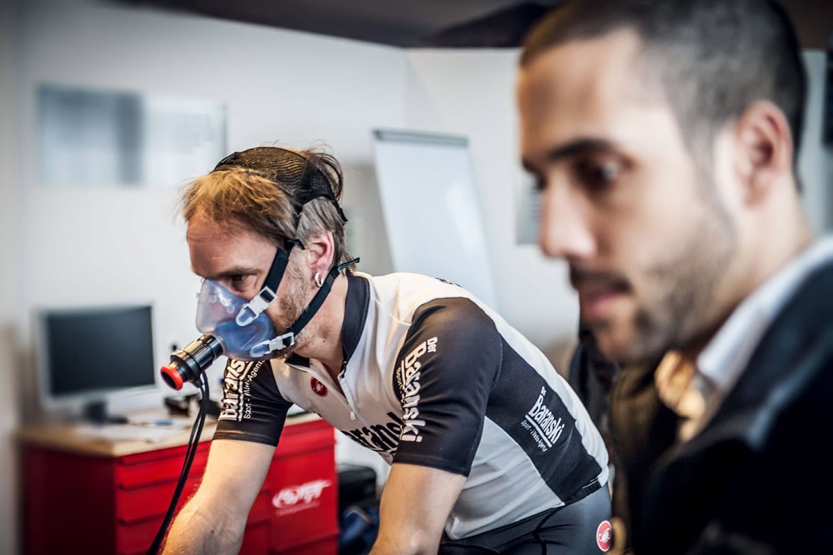Radsportler mit Atemmaske bei der Leistungsdiagnostik, betreut von einem HYCYS-Coach